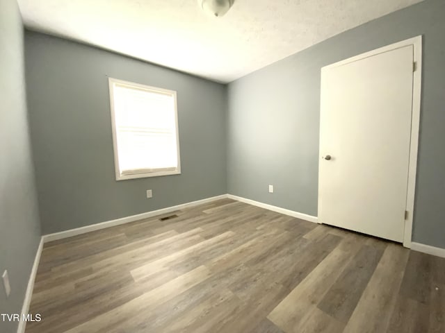 empty room with wood finished floors, visible vents, and baseboards