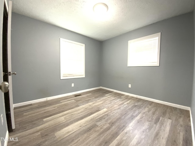empty room featuring a textured ceiling, wood finished floors, plenty of natural light, and baseboards