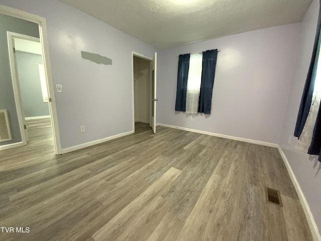 unfurnished bedroom with wood finished floors, visible vents, a closet, and baseboards