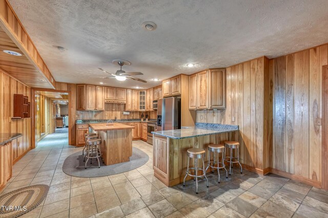 1010 Heaton Creek Rd, Roan Mountain, TN 37687 - kitchen featuring baseboards, a kitchen bar, a ceiling fan, wooden walls, and appliances with stainless steel finishes