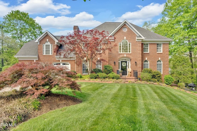 view of front of property featuring brick siding, a chimney, a front yard, and a shingled roof