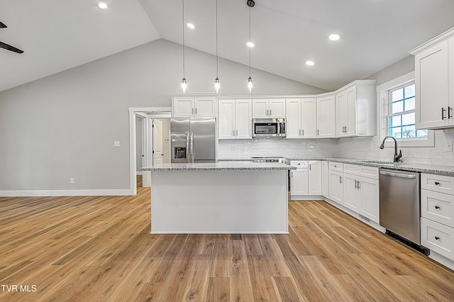 kitchen with light stone counters, white cabinets, a sink, appliances with stainless steel finishes, and a kitchen island