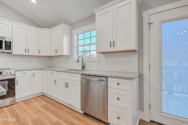 kitchen with light wood-style flooring, stainless steel appliances, vaulted ceiling, white cabinets, and a sink