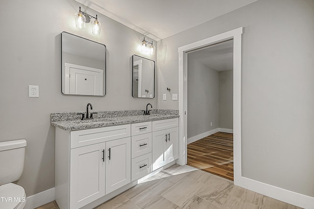 bathroom featuring baseboards, toilet, double vanity, and a sink