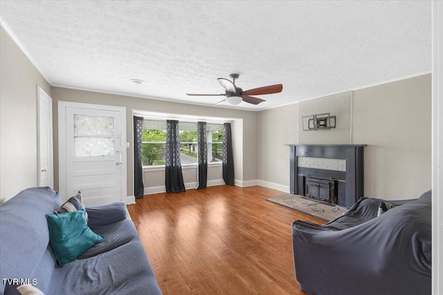 living room featuring a textured ceiling, a fireplace with raised hearth, baseboards, wood finished floors, and a ceiling fan