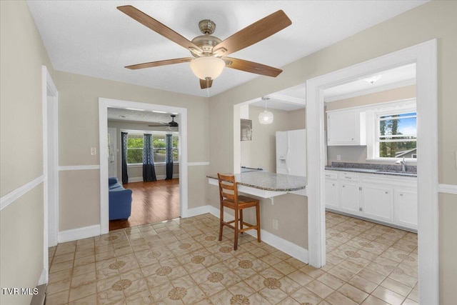 kitchen featuring dark stone counters, a sink, white refrigerator with ice dispenser, a ceiling fan, and white cabinets