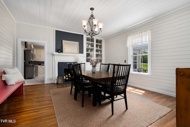 dining room featuring a chandelier, wooden walls, ornamental molding, a fireplace, and wood finished floors