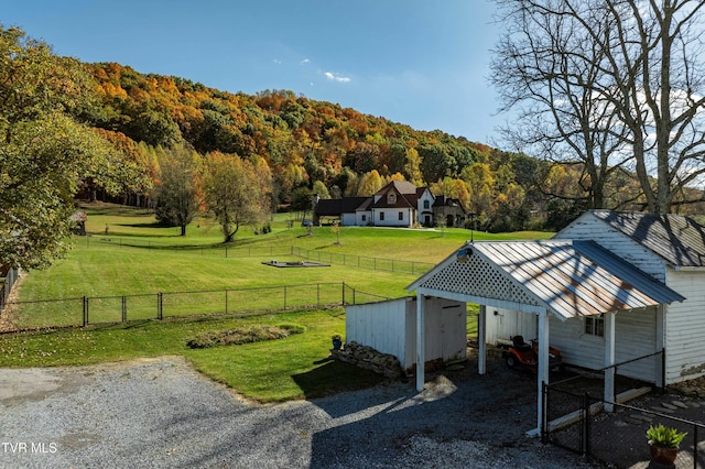 view of community featuring a wooded view, a detached carport, a fenced backyard, and a yard