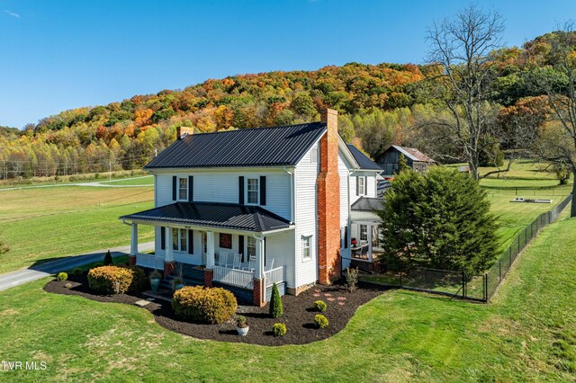 view of front of home featuring a chimney, fence, a porch, and a wooded view