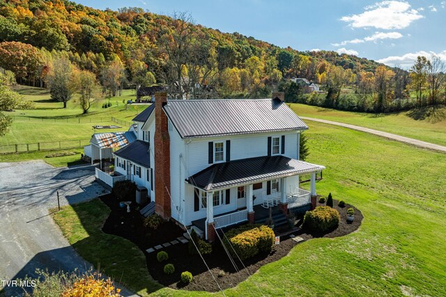 exterior space featuring metal roof, a forest view, covered porch, and a chimney
