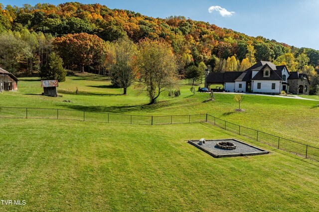 exterior space with fence, a fire pit, a rural view, and a view of trees