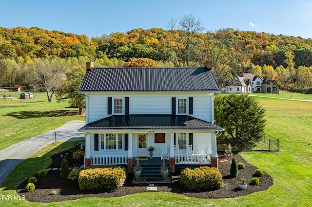 view of front of property with a chimney, a front lawn, metal roof, and a view of trees