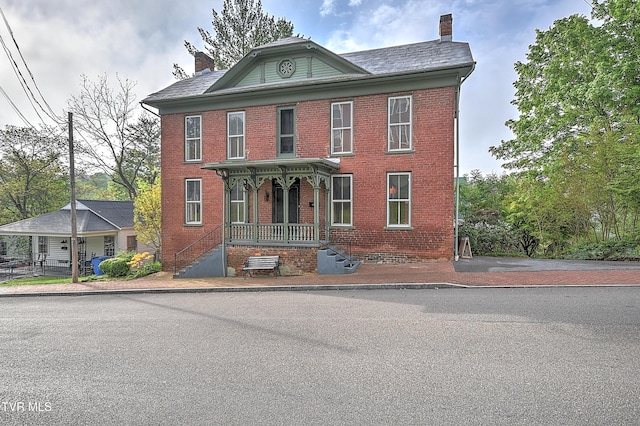 view of front of house with covered porch, a chimney, and brick siding