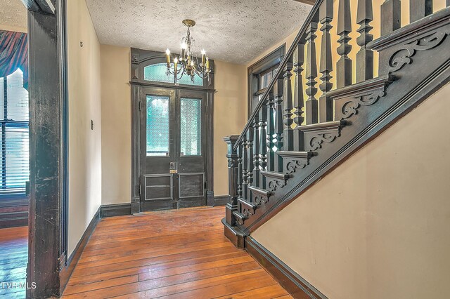 foyer entrance with baseboards, stairs, a chandelier, and hardwood / wood-style floors