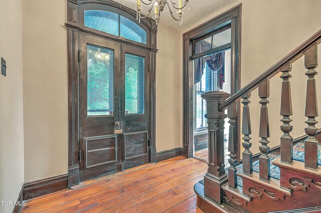 entryway featuring a textured ceiling, baseboards, an inviting chandelier, stairs, and hardwood / wood-style floors