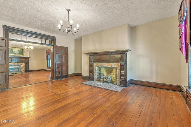 unfurnished living room with a fireplace with raised hearth, a chandelier, and hardwood / wood-style floors