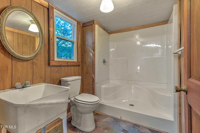 full bathroom with wood walls, toilet, walk in shower, a sink, and stone finish flooring