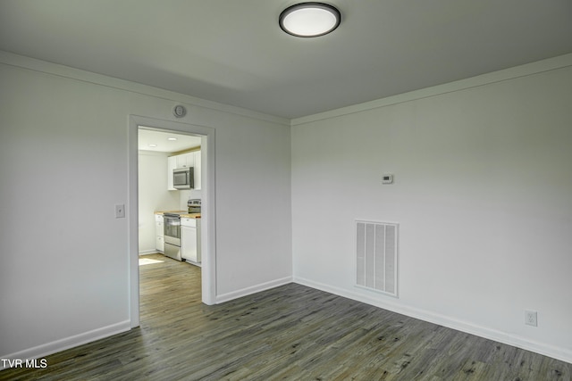 spare room featuring baseboards, dark wood-style floors, and visible vents