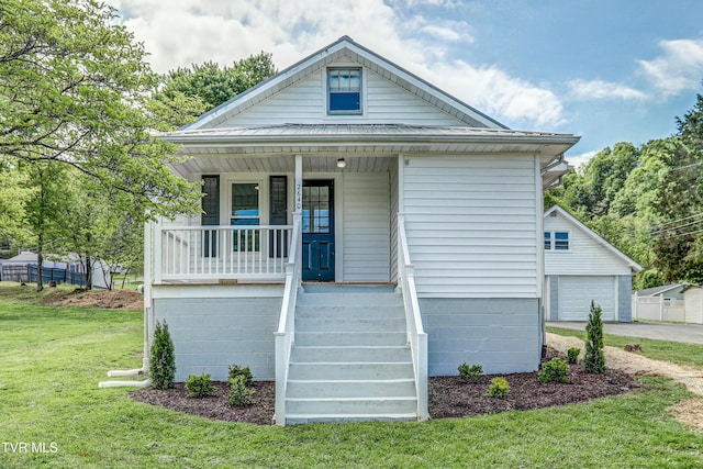 view of front facade with a porch, metal roof, a front yard, and a detached garage