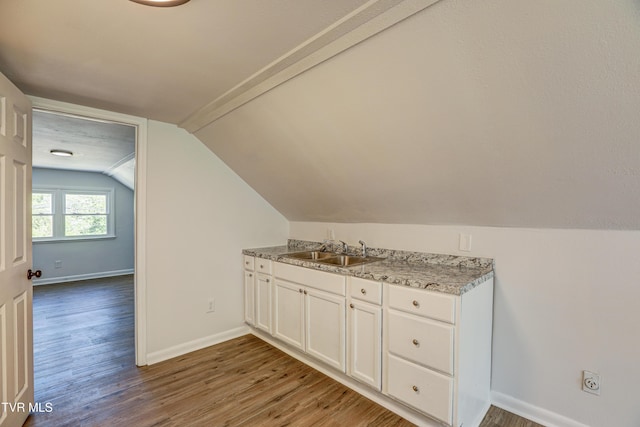 additional living space with baseboards, vaulted ceiling, a sink, and wood finished floors