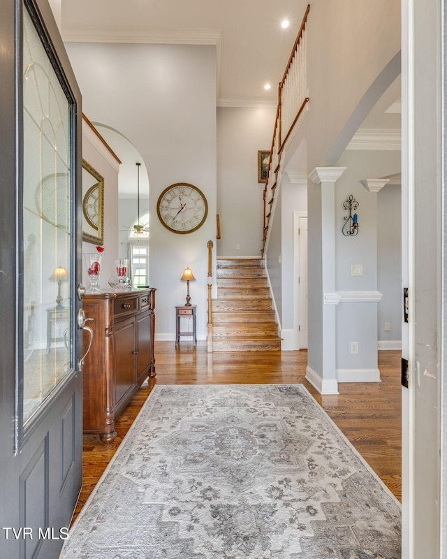 foyer entrance with wood finished floors, stairs, arched walkways, and crown molding
