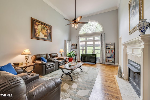 living area featuring a fireplace, ceiling fan, crown molding, and light wood finished floors