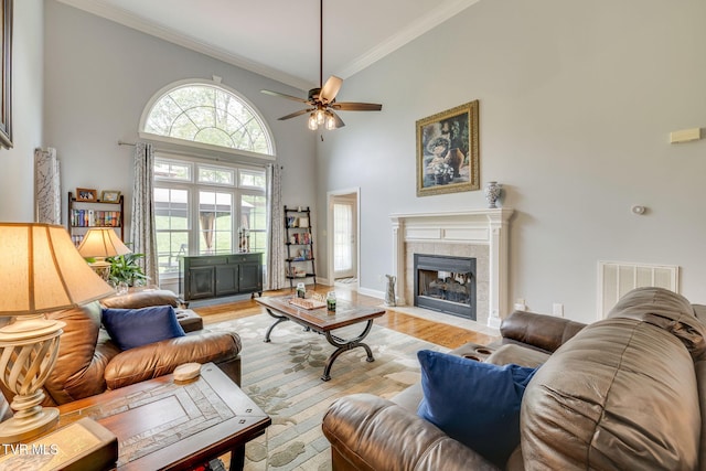 living room with light wood-style flooring, visible vents, a ceiling fan, crown molding, and a towering ceiling