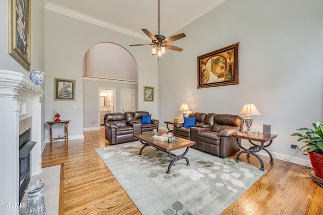 living room with arched walkways, light wood-style flooring, a fireplace, a ceiling fan, and crown molding