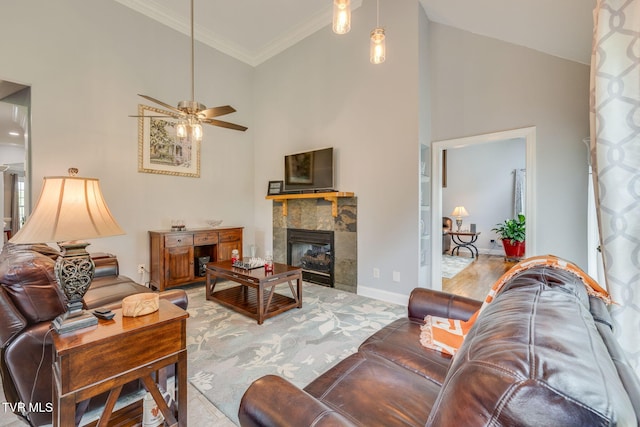 living area with a tiled fireplace, ceiling fan, crown molding, and a towering ceiling