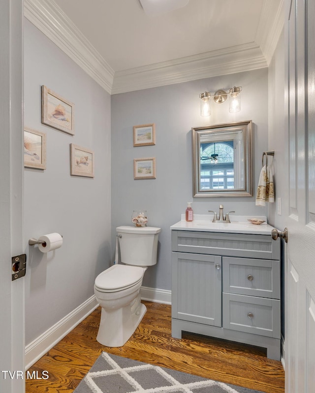 bathroom with crown molding, baseboards, toilet, wood finished floors, and vanity