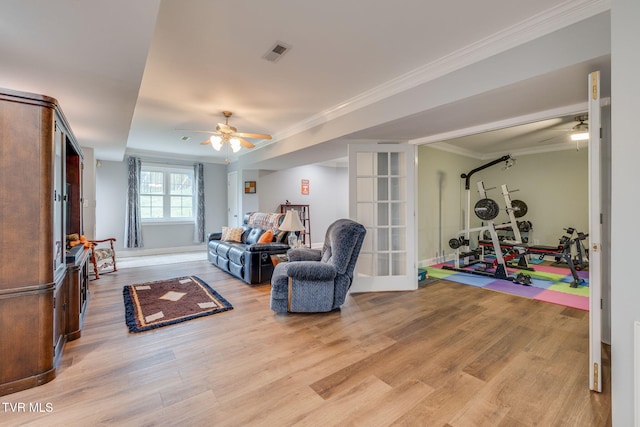living room featuring visible vents, baseboards, light wood-type flooring, ornamental molding, and a ceiling fan