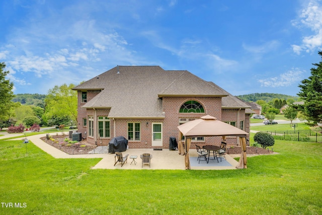 rear view of property featuring a lawn, brick siding, a gazebo, and a patio area