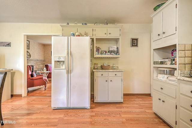 kitchen with white refrigerator with ice dispenser, open shelves, light stone countertops, light wood-style floors, and white cabinetry