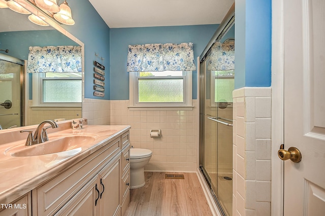bathroom with wood finished floors, a wainscoted wall, a healthy amount of sunlight, and tile walls