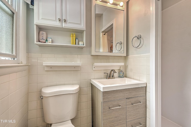 bathroom with toilet, tile walls, plenty of natural light, and vanity