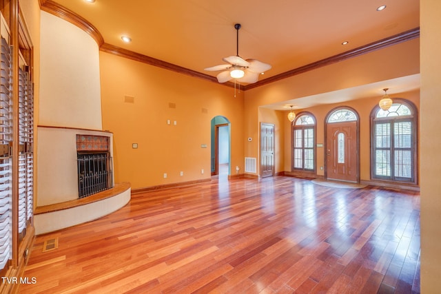 unfurnished living room featuring a fireplace with raised hearth, visible vents, ceiling fan, and ornamental molding