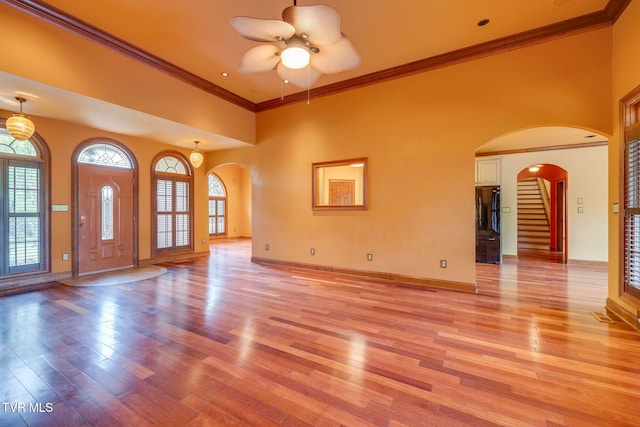 unfurnished living room with light wood-type flooring, arched walkways, ceiling fan, and ornamental molding