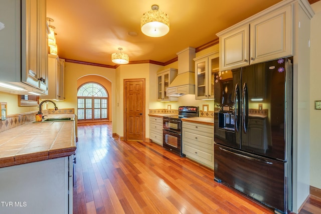 kitchen featuring a sink, arched walkways, black appliances, ornamental molding, and custom exhaust hood