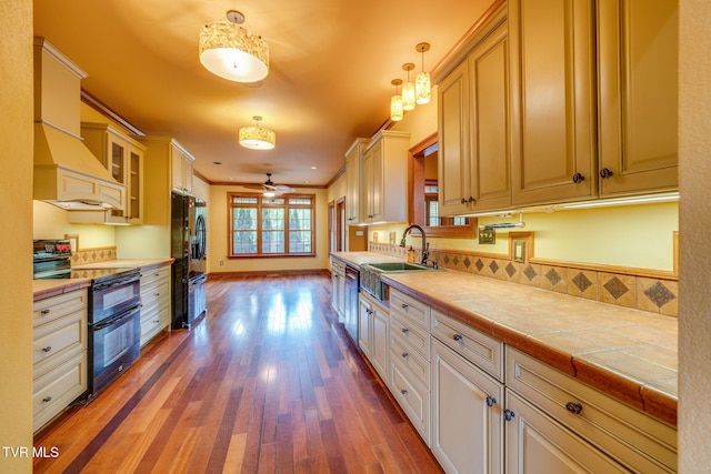 kitchen featuring wood finished floors, glass insert cabinets, black appliances, a sink, and a ceiling fan