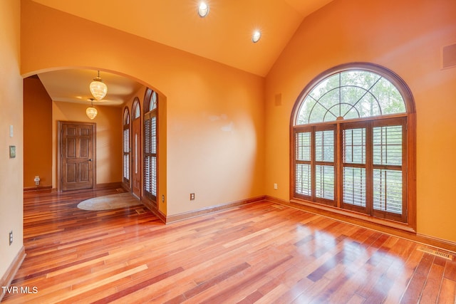 entryway with visible vents, baseboards, arched walkways, light wood-type flooring, and high vaulted ceiling