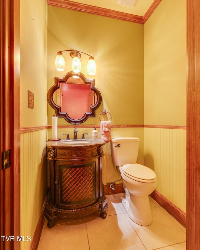 half bath with toilet, a wainscoted wall, tile patterned flooring, and vanity