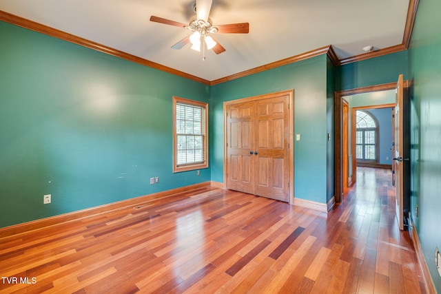 unfurnished bedroom featuring a closet, a ceiling fan, baseboards, ornamental molding, and wood finished floors