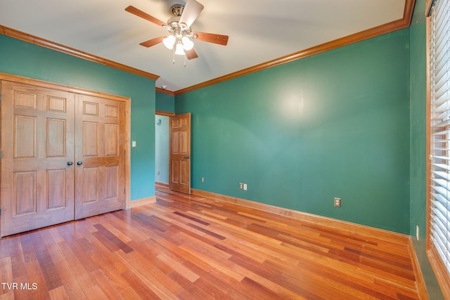 unfurnished bedroom featuring a closet, crown molding, a ceiling fan, baseboards, and wood finished floors
