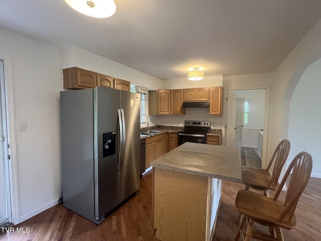 kitchen featuring a sink, stainless steel appliances, under cabinet range hood, a kitchen island, and arched walkways