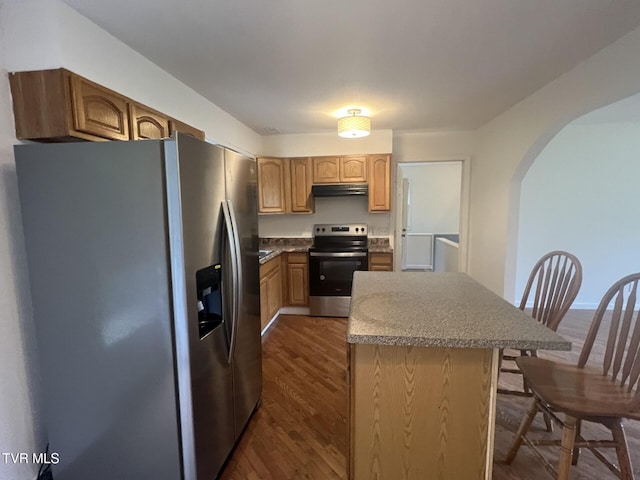 kitchen featuring arched walkways, under cabinet range hood, appliances with stainless steel finishes, a center island, and dark wood-type flooring