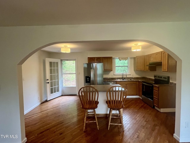 kitchen with dark wood-style flooring, stainless steel appliances, under cabinet range hood, dark countertops, and arched walkways
