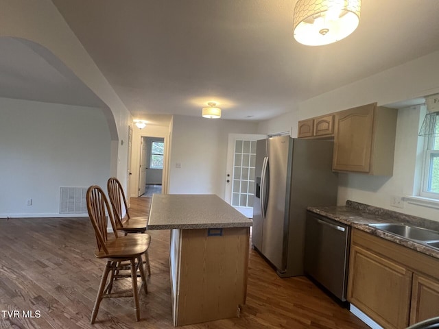 kitchen with arched walkways, appliances with stainless steel finishes, a kitchen island, a sink, and dark wood-style floors