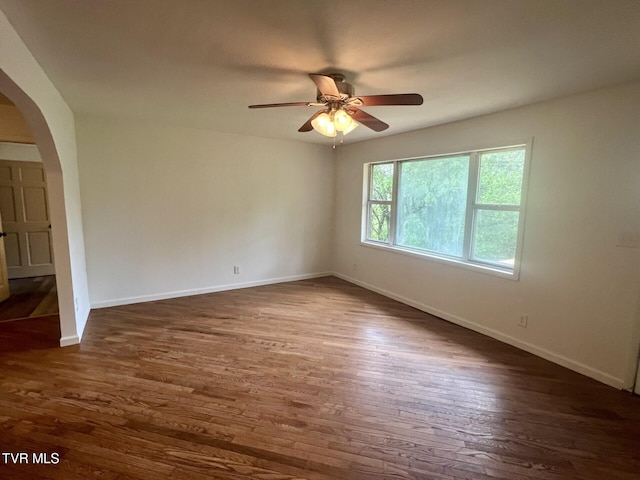 empty room featuring arched walkways, dark wood-style flooring, and a ceiling fan