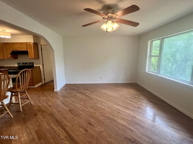 interior space with baseboards, arched walkways, a ceiling fan, and wood-type flooring