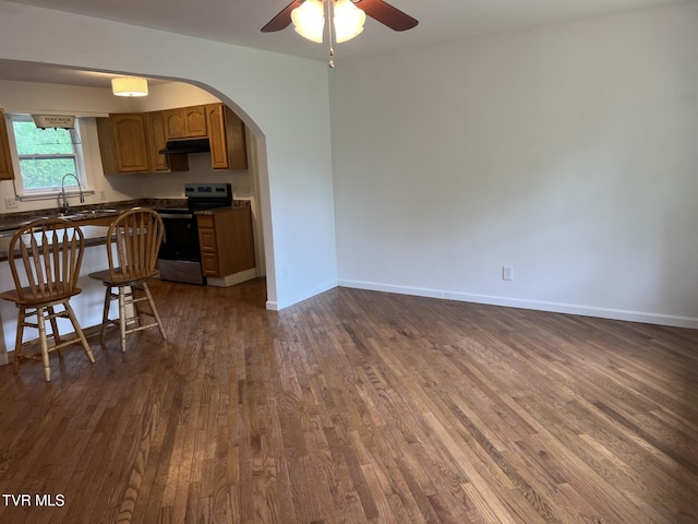 interior space with dark wood-style floors, under cabinet range hood, dark countertops, arched walkways, and electric range